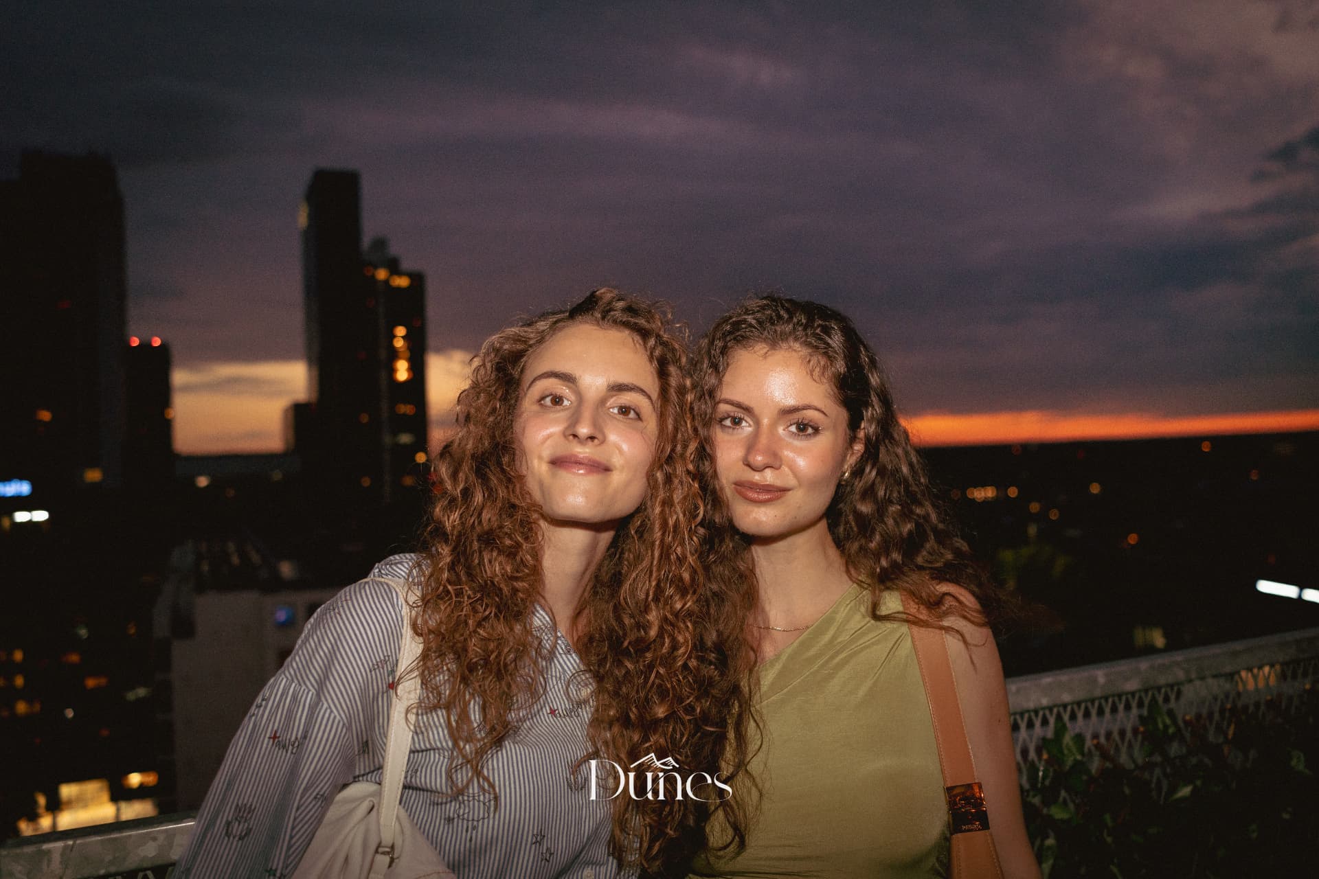 Two guests at golden hour on a rooftop during a Dunes event with the city skyline behind them